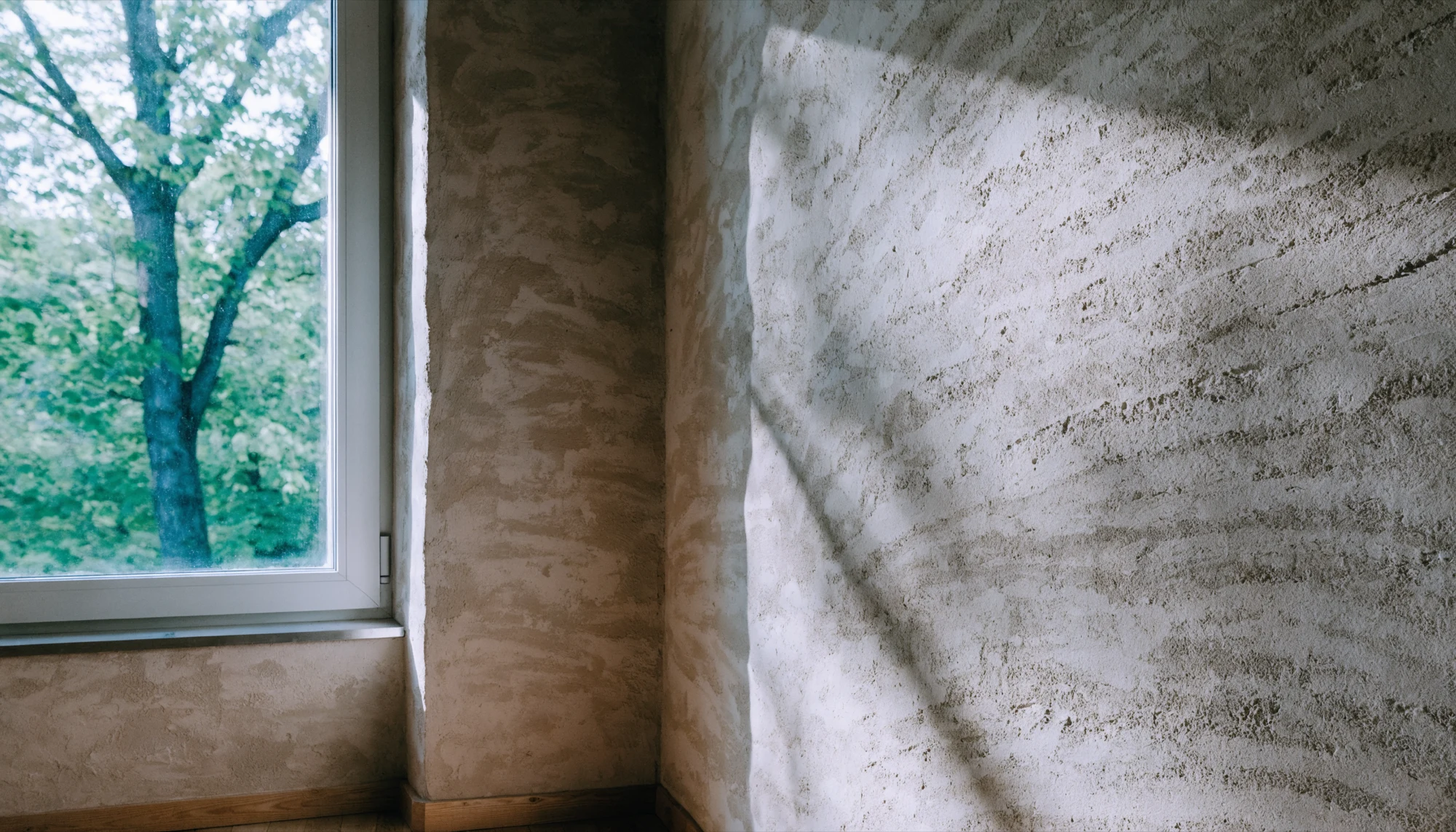 Ruhige Wandfläche mit Fenster, Ecke, Sockel und Putz, den typischen Stellen für Feuchtigkeit