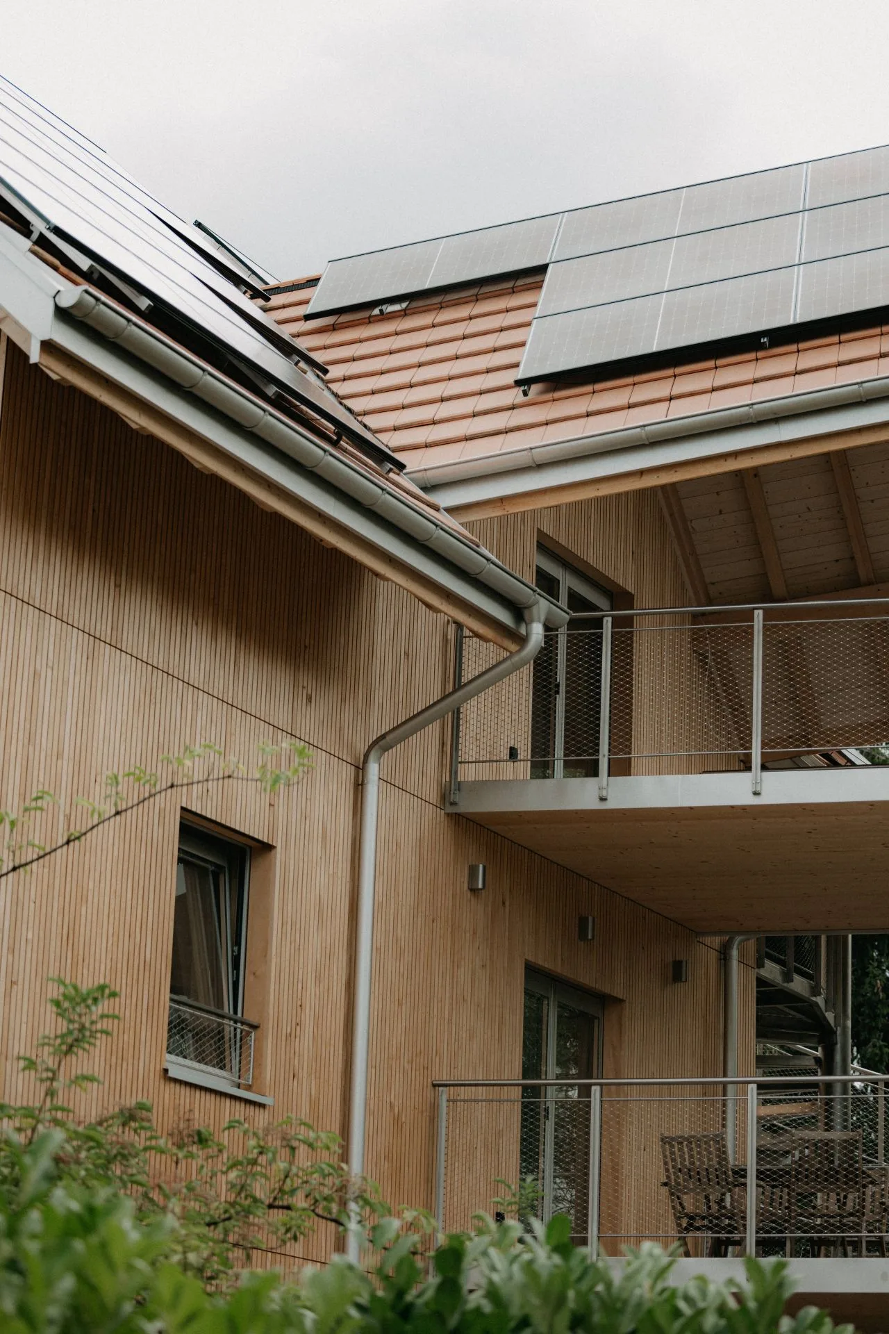 Holzfassade mit Balkonen und Solardach, von unten gesehen.